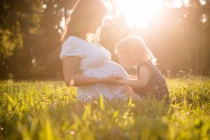 pregnant woman is sitting in the grass with her daughter